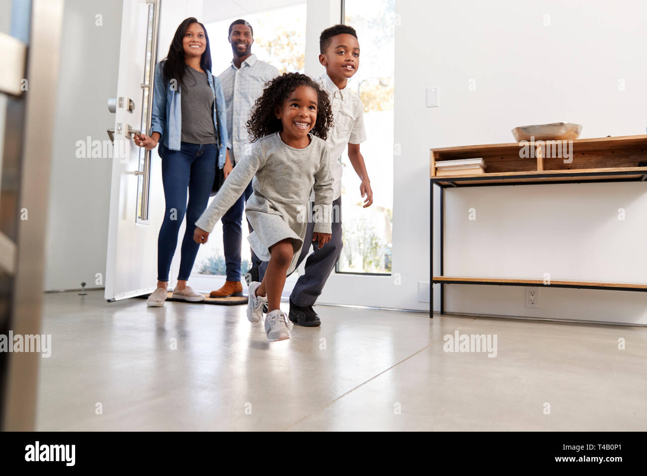 Les parents et les enfants de rentrer chez eux l'ouverture de porte avant et exécute à l'intérieur Banque D'Images