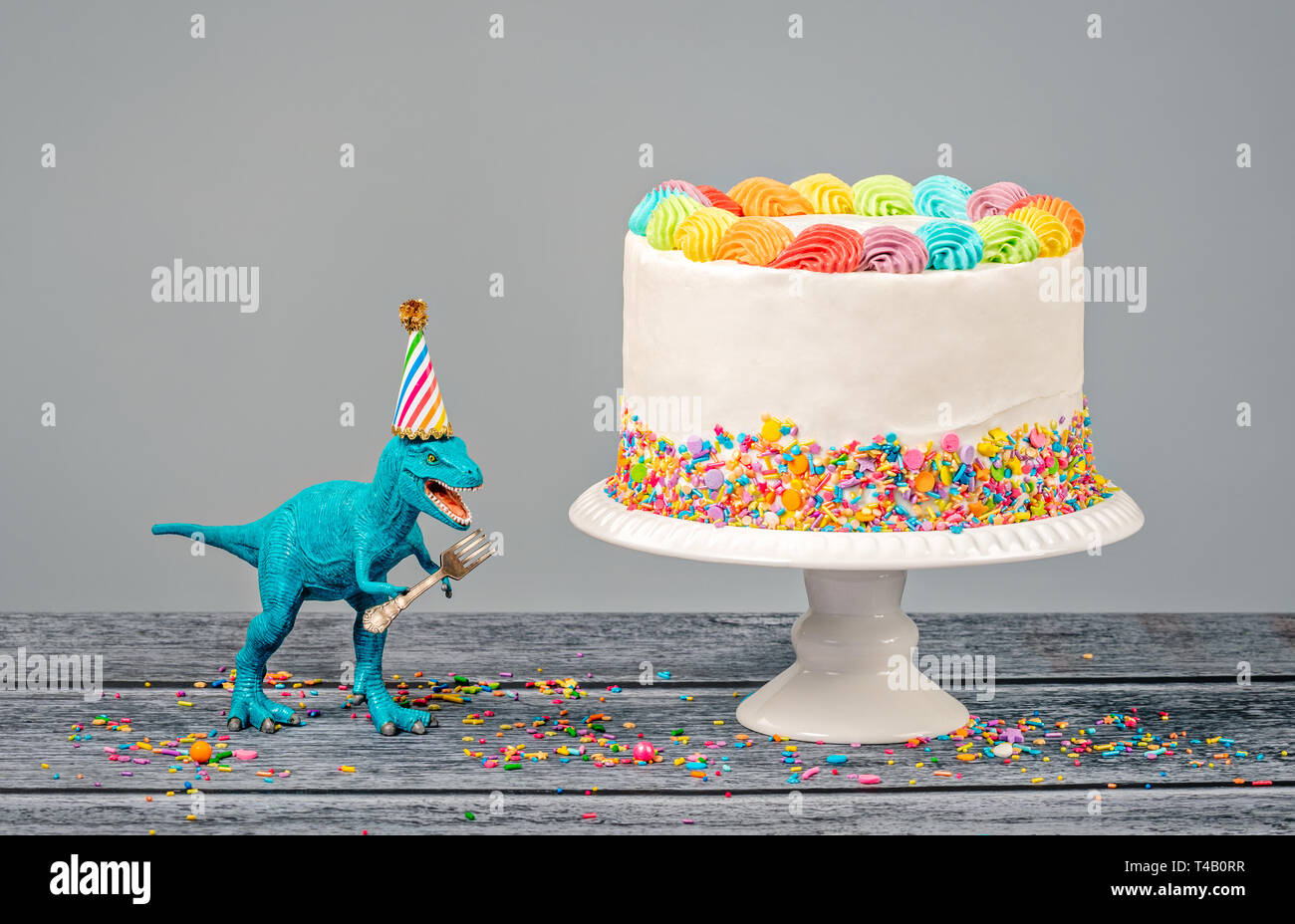 Hungry Toy Dinosaur Portant Un Chapeau Et Tenant Une Fourche A Cote D Un Gateau D Anniversaire Sur Fond Gris Photo Stock Alamy