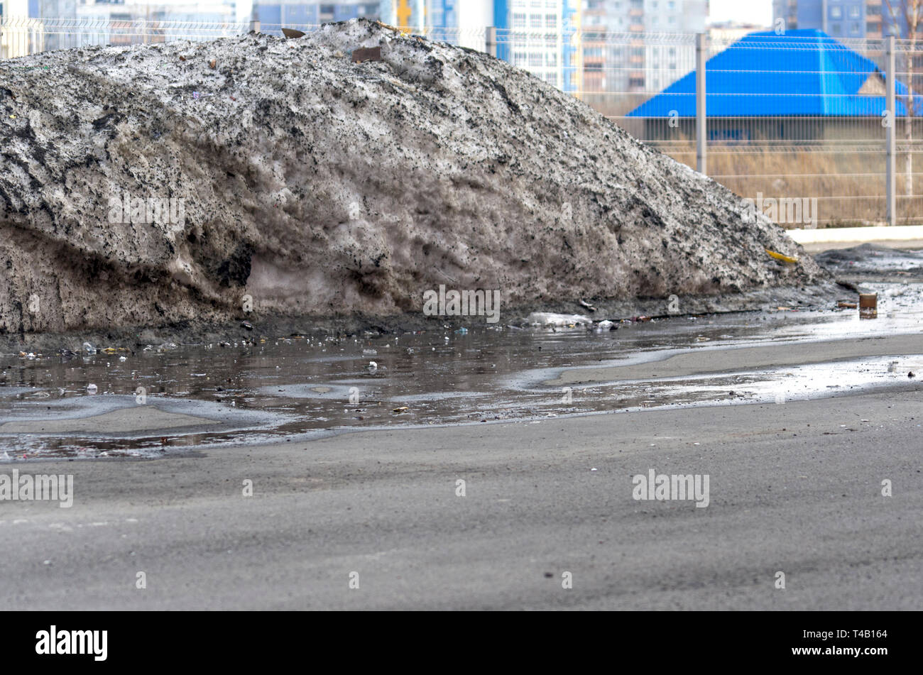 Gros tas de neige sale dans un parking de flaques et les débris recueillis au cours de l'hiver. Journée de printemps chaud Banque D'Images