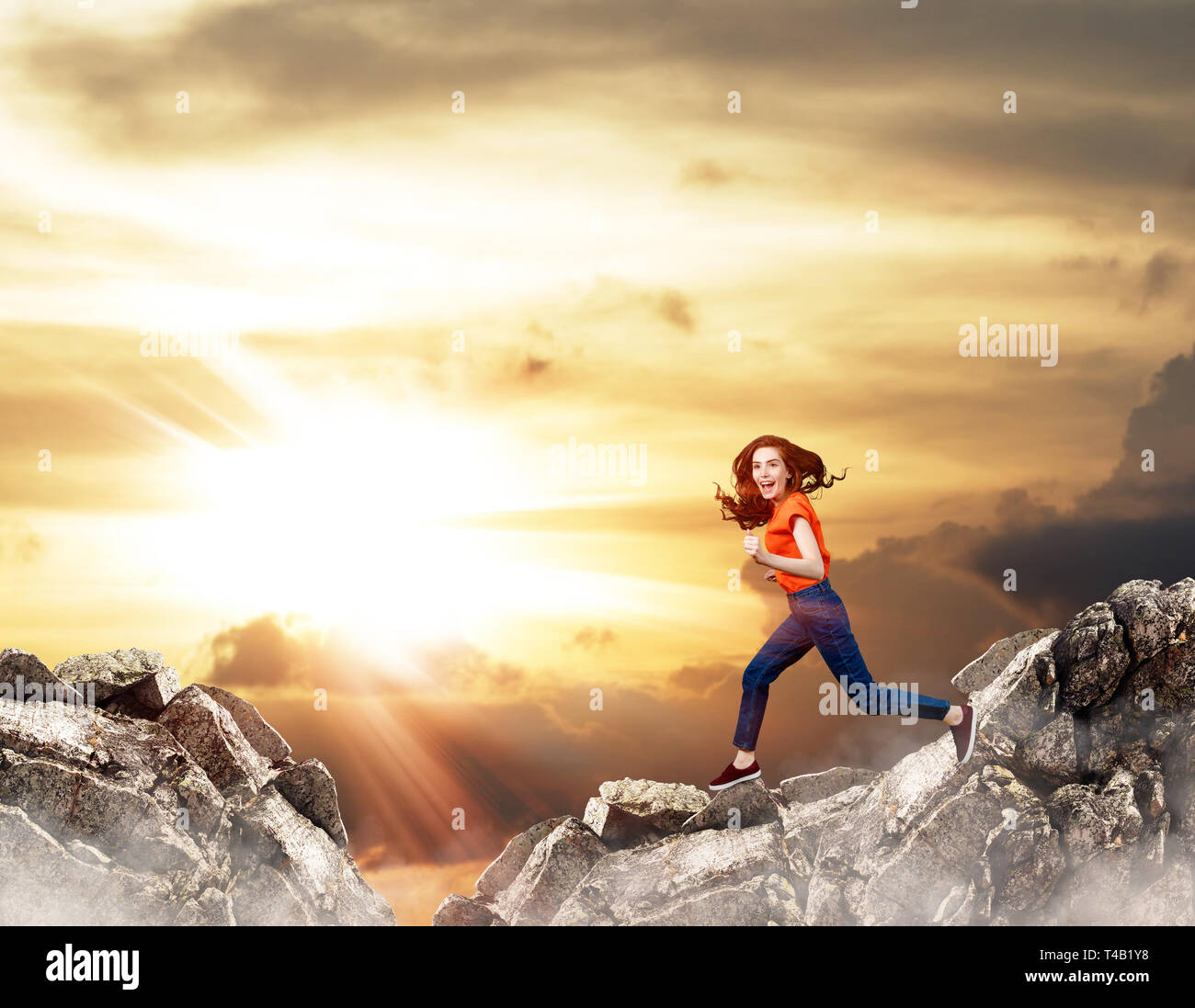 Femme rousse saute sur falaise sur fond de ciel bleu. Banque D'Images