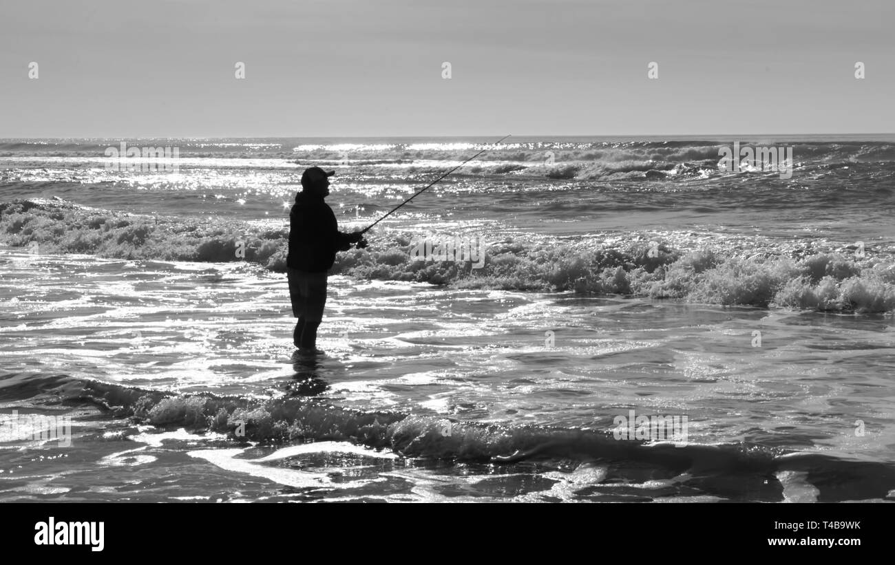 Silhouette de pêcheur au bord de l'Atlantique de patauger dans l'eau en noir et blanc. Banque D'Images