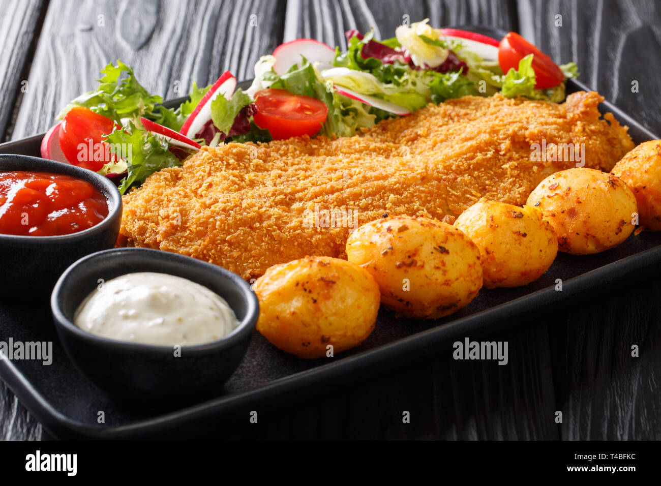 Filet de morue servi dans de la panure avec pommes de terre et salade de légumes frais sur une assiette sur la table horizontale. Banque D'Images