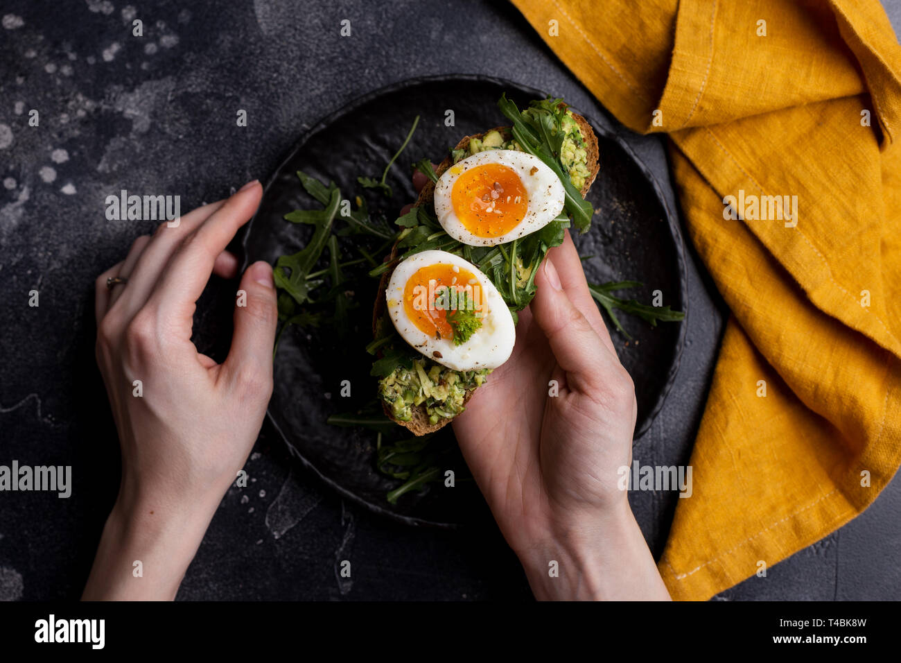 Toast aux œufs et d'avocat sur pain in women's hands sur fond noir. Vue de dessus, tablette, télévision lay. Concept de petit-déjeuner sain. Photo de vie Banque D'Images Toast aux œufs et d'avocat sur pain in women's hands sur fond noir. Vue de dessus, tablette, télévision lay. Concept de petit-déjeuner sain. Photo de vie Banque D'Images
