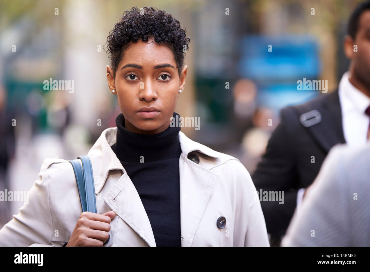 Young adult woman wearing pullover à col roulé et mackintosh marcher dans une rue animée de Londres, vue de face Banque D'Images