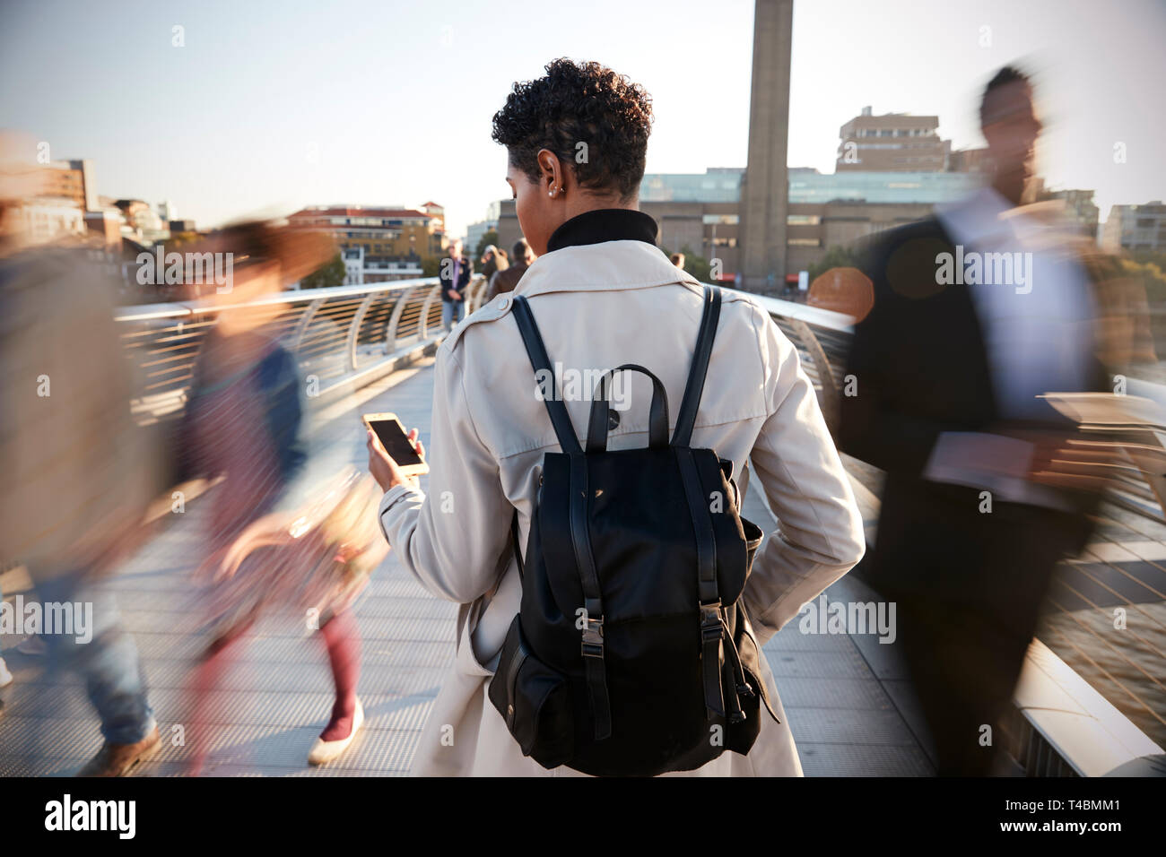 Vue arrière de jeune adulte femme debout sur le pont du Millénaire, à Londres, à l'aide de smartphone, le motion blur Banque D'Images