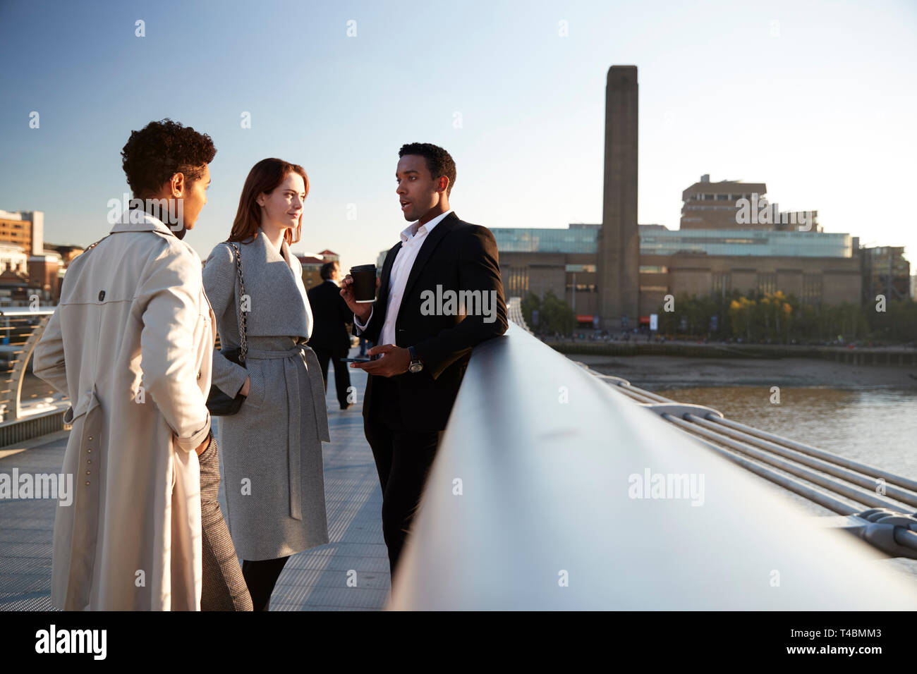 Vue de côté de trois collègues d'affaires millénaire conversation sur Millennium Bridge, Londres, selective focus Banque D'Images