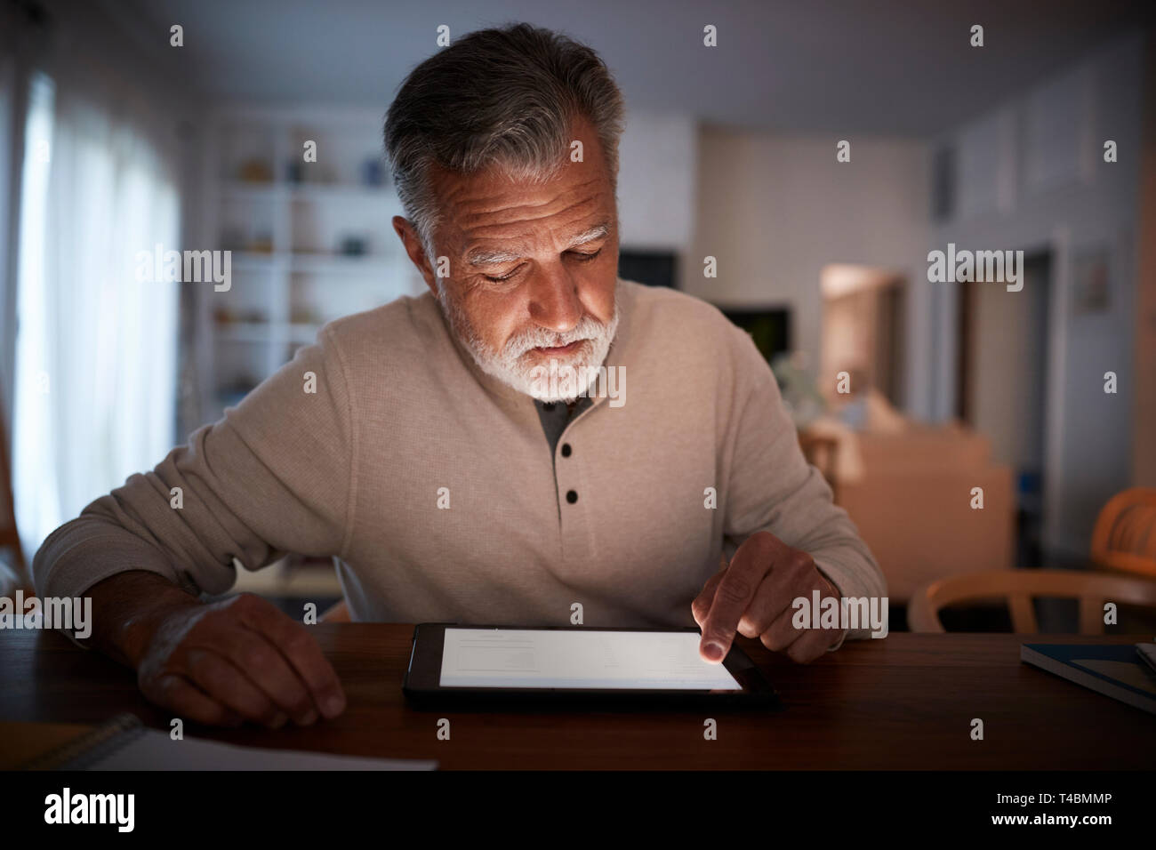 Senior homme assis à une table à l'aide d'un ordinateur tablette à la maison le soir, Close up Banque D'Images