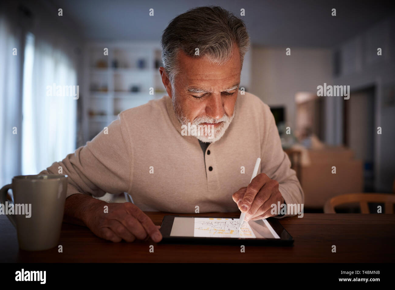 Senior homme est assis à table à l'aide du stylet et tablette ordinateur à la maison le soir, Close up Banque D'Images
