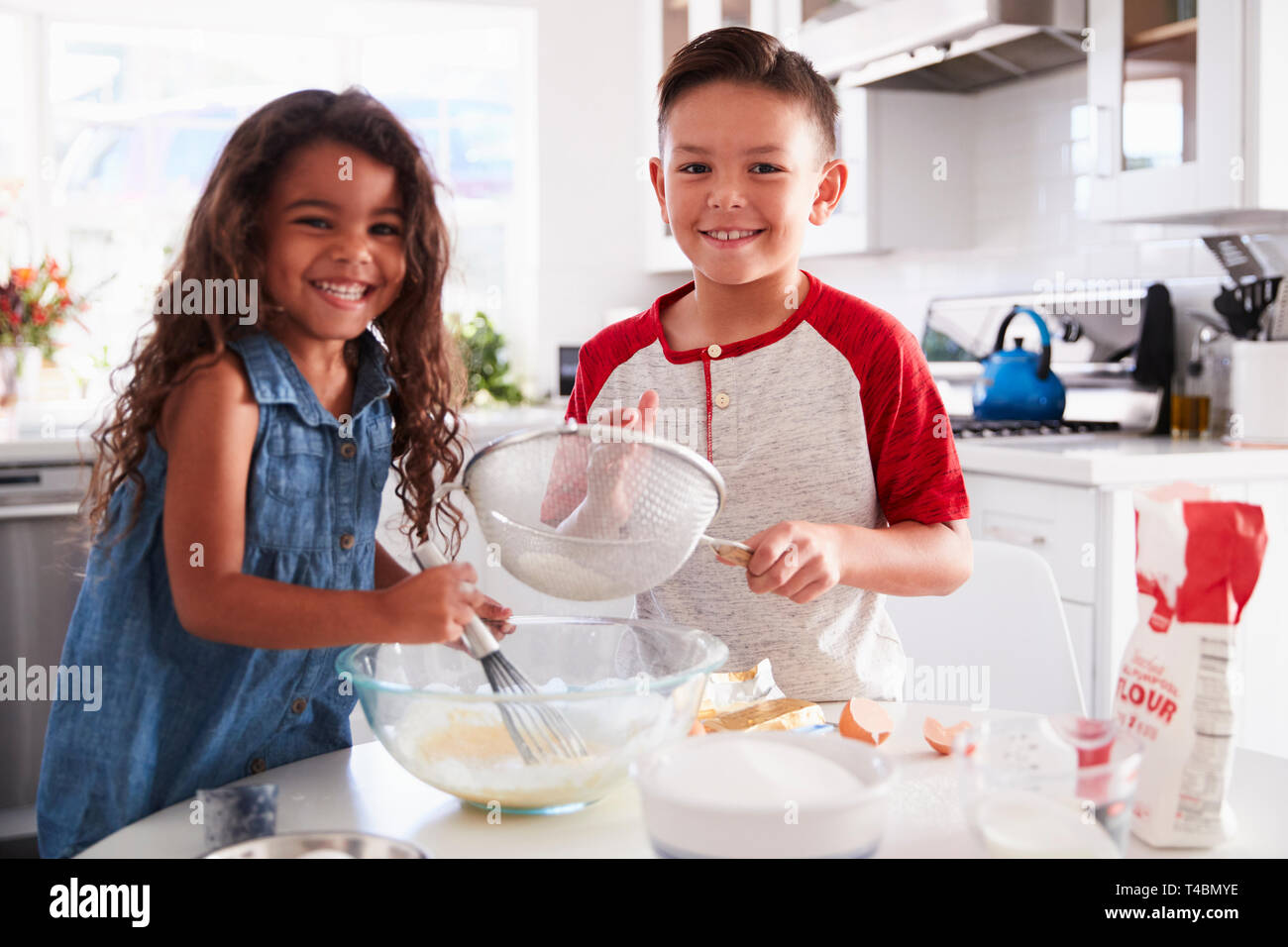 Frère et soeur de la préparation du mélange à gâteau ensemble à la table de cuisine à la recherche d'appareil photo, jusqu'à la taille Banque D'Images