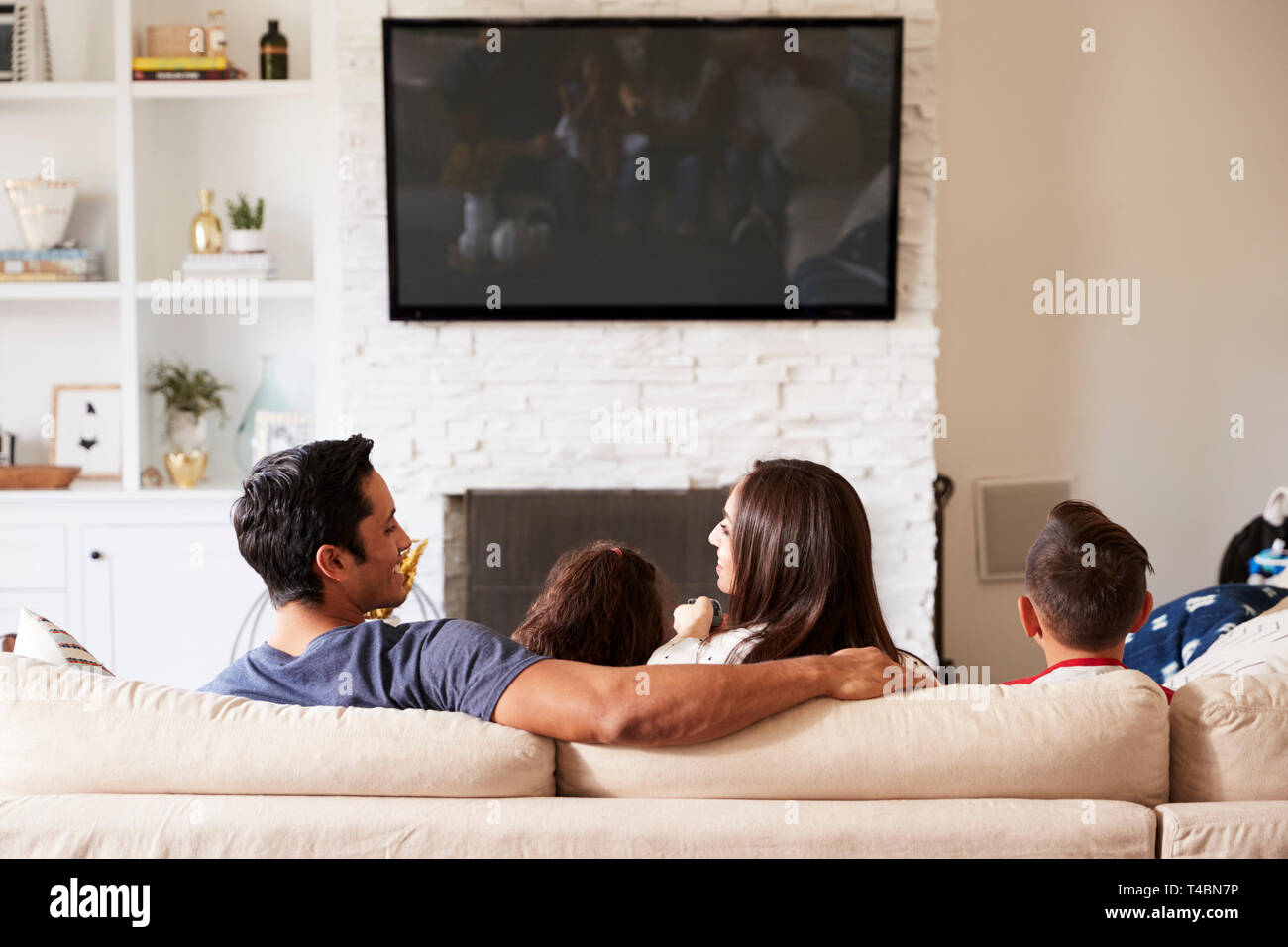 Vue arrière de l'Hispanique jeune famille de quatre assis sur le canapé à regarder la télévision, à la maman à papa Banque D'Images