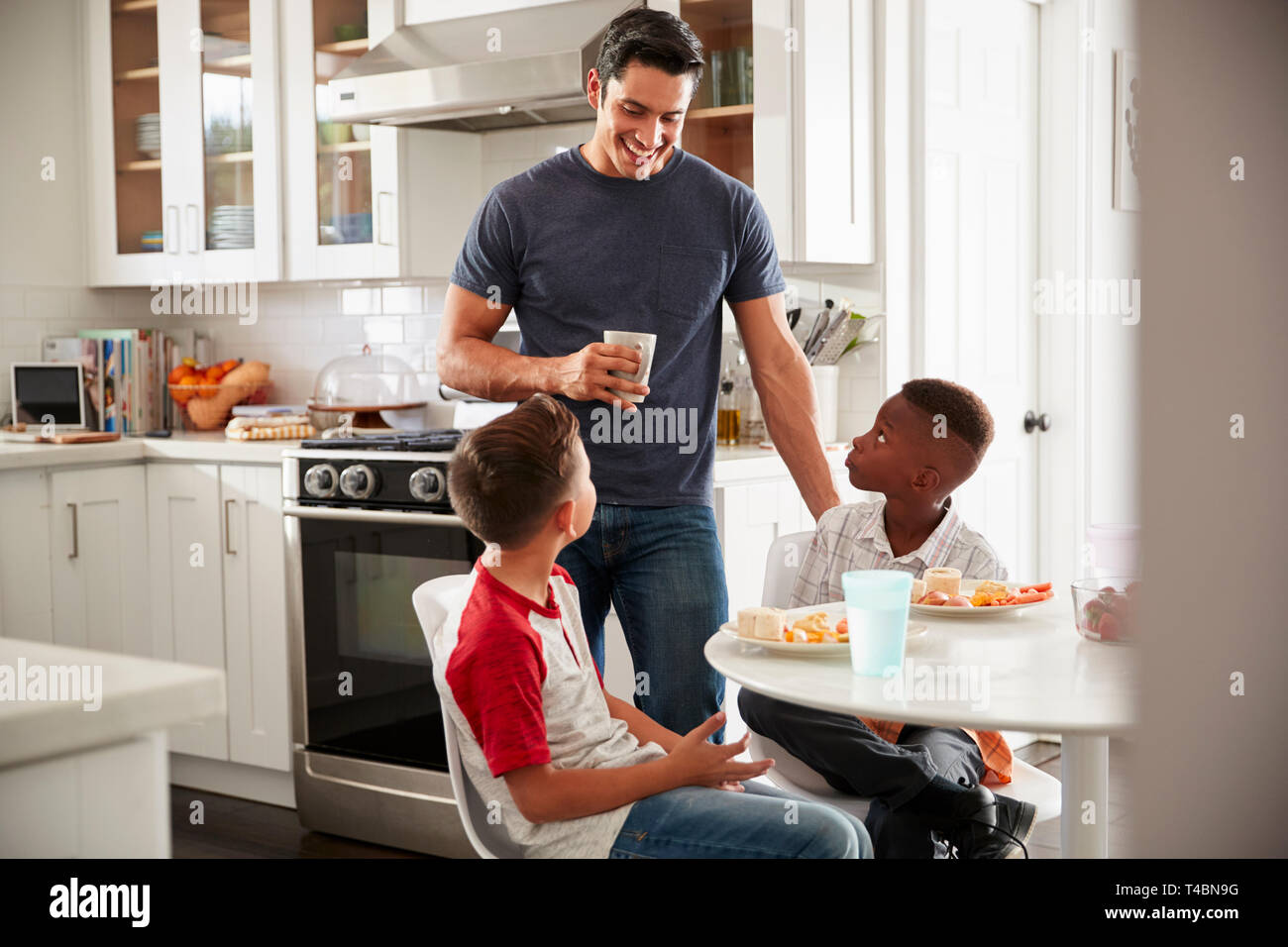Papa debout dans la cuisine à parler avec son fils et un ami, qui est plus pour une playdate Banque D'Images