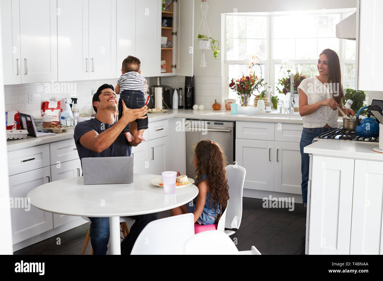 Young Hispanic family dans leur cuisine, papa holding baby dans l'air, maman de la cuisson à la cuisson Banque D'Images