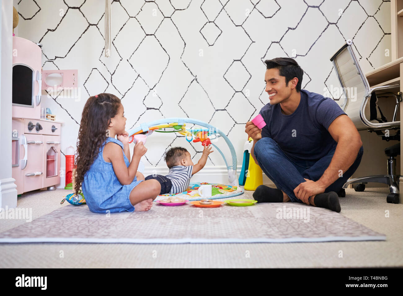 Young Girl playing tea party avec papa, assis sur le plancher, frère bébé sur un tapis de jeu à côté d'eux Banque D'Images