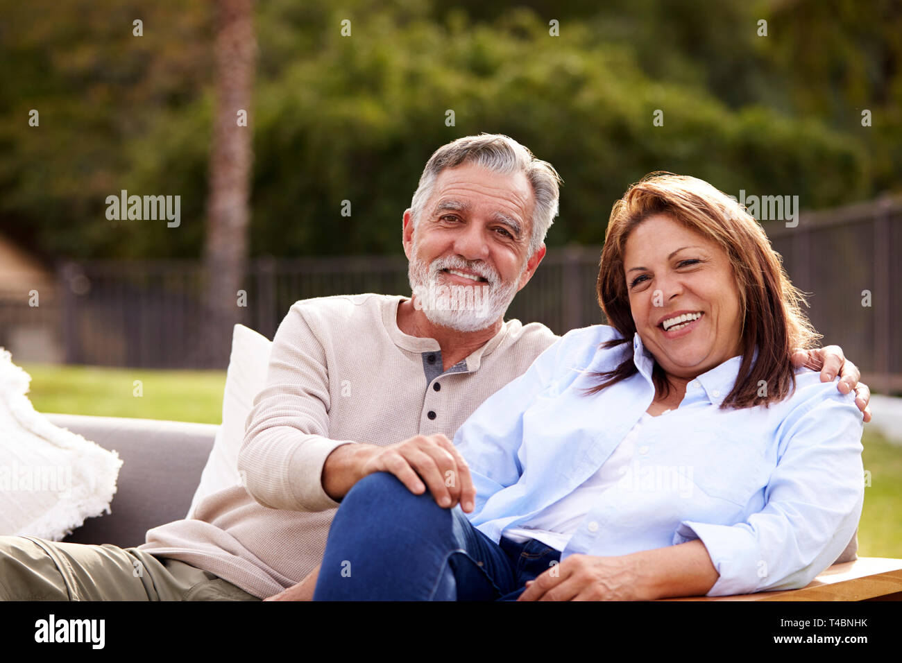 Senior couple sitting ensemble sur un siège dans le jardin souriant pour appareil photo, vue de face Banque D'Images