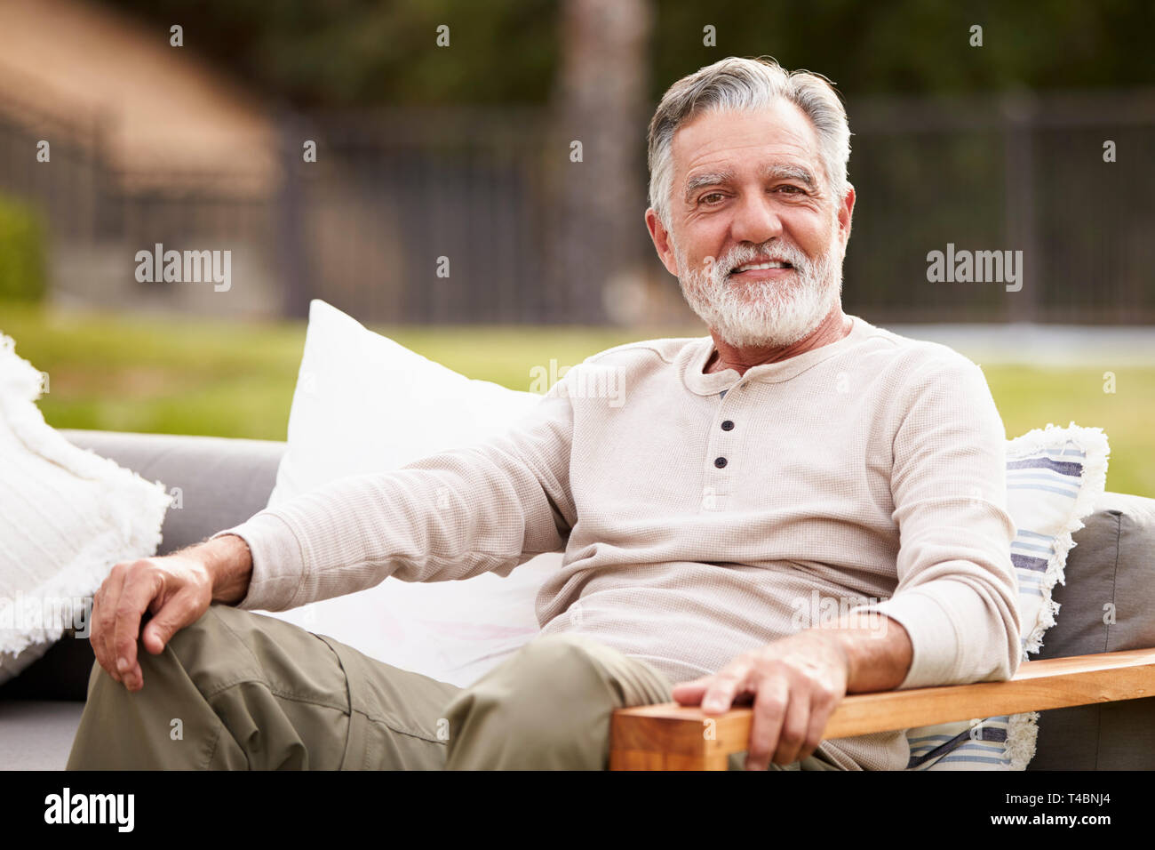 Happy senior man assis sur un siège dans le jardin souriant pour appareil photo, Close up Banque D'Images