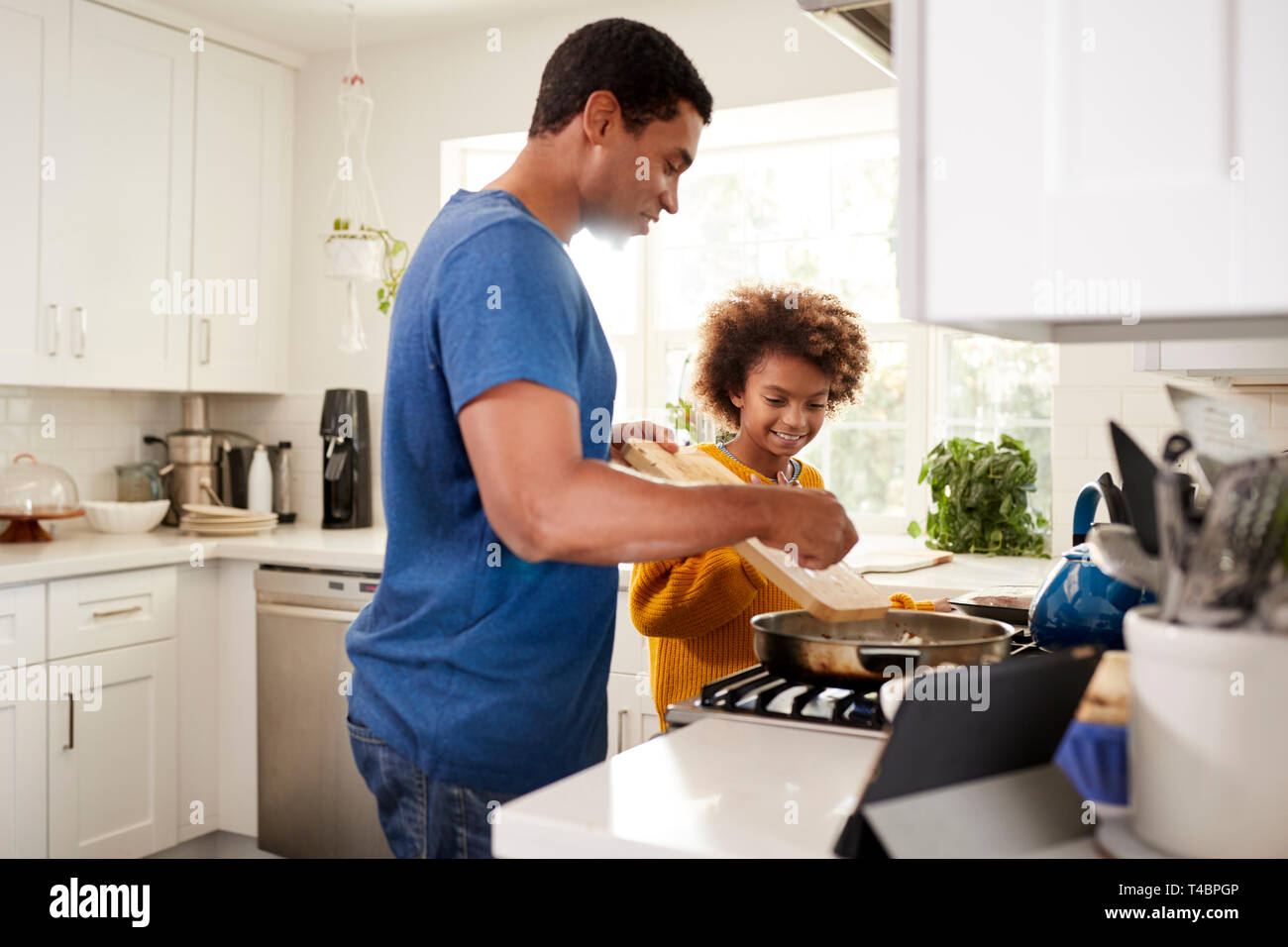 Pré-ado fille et son père debout à plaque de cuisson dans la cuisine la préparation des aliments dans une poêle, à la suite d'une recette sur un ordinateur tablette, rétroéclairé Banque D'Images