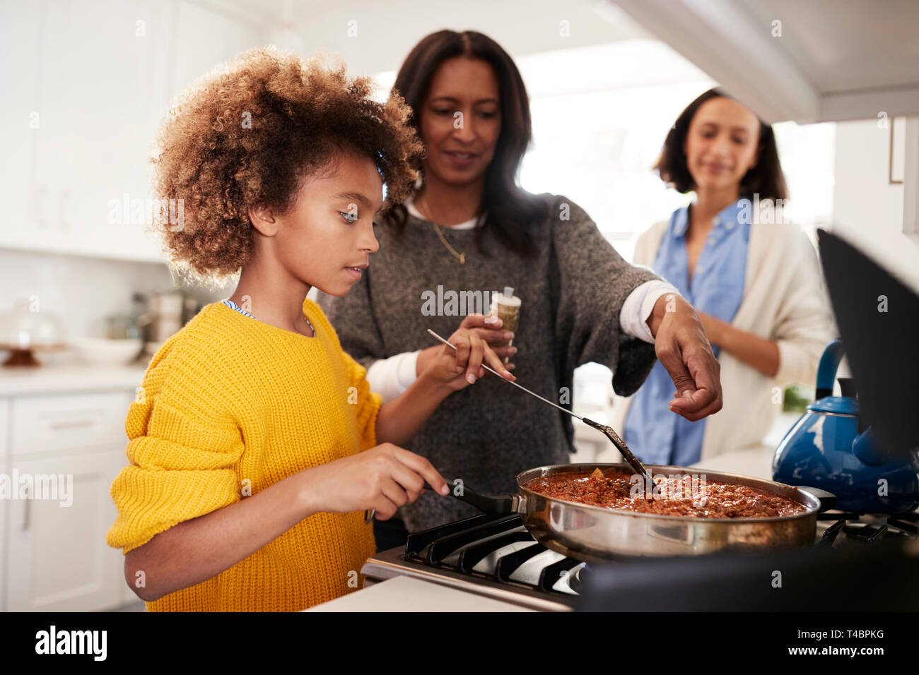 Pré-ado fille noire debout à la plaque de cuisson dans la cuisine préparer la nourriture avec sa grand-mère et mère, Close up, selective focus Banque D'Images