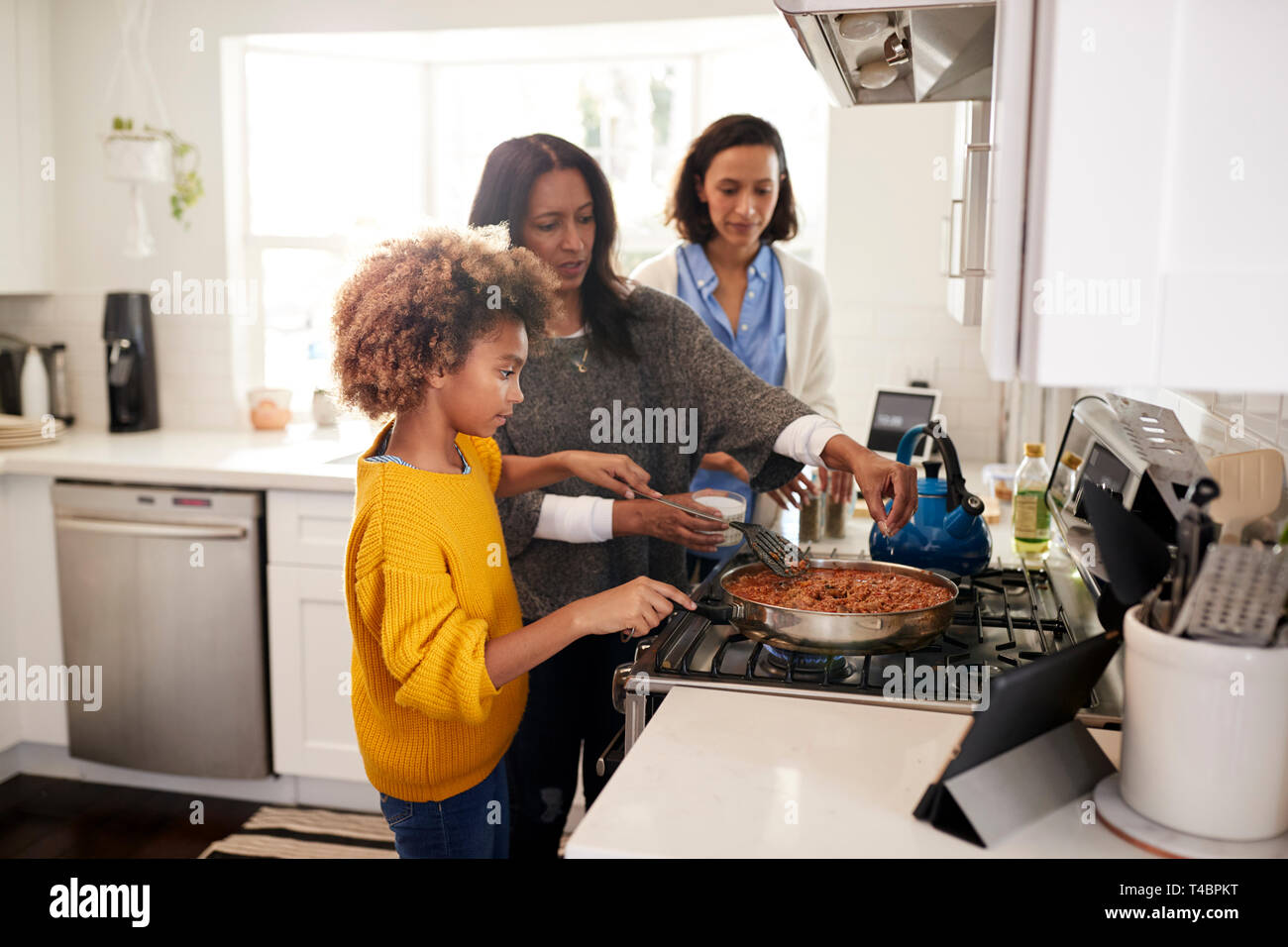 Pré-ado fille noire debout à la plaque de cuisson dans la cuisine préparer la nourriture avec sa grand-mère et mère, selective focus Banque D'Images