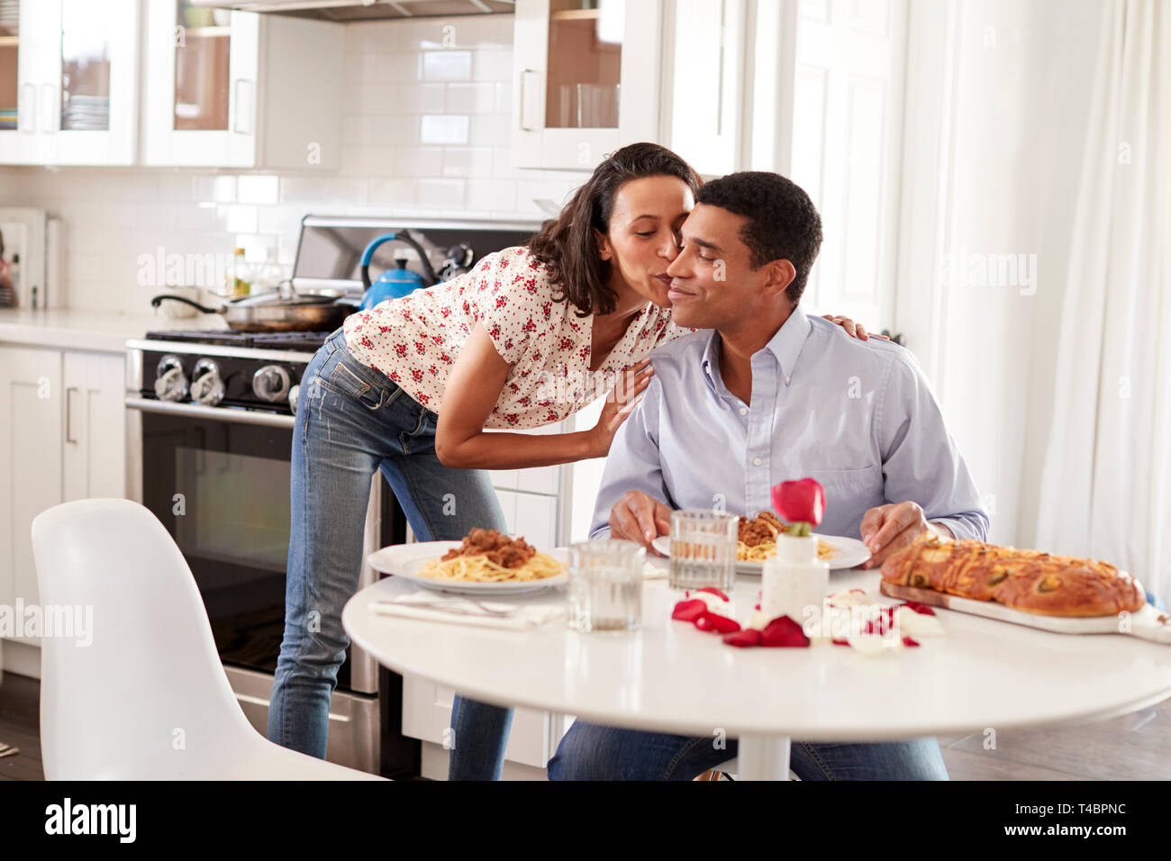 Young adult woman kissing her partner, assis à la table dans la cuisine pour un dîner romantique, selective focus Banque D'Images