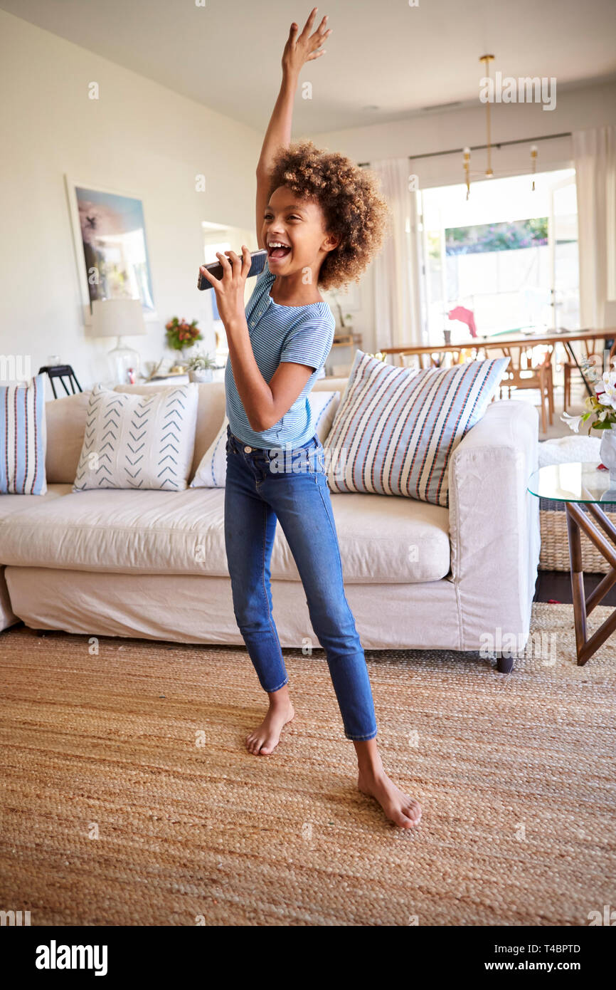 Pré-ado fille danser et chanter dans la salle de séjour à la maison en utilisant son téléphone comme un microphone, pleine longueur, verticale Banque D'Images