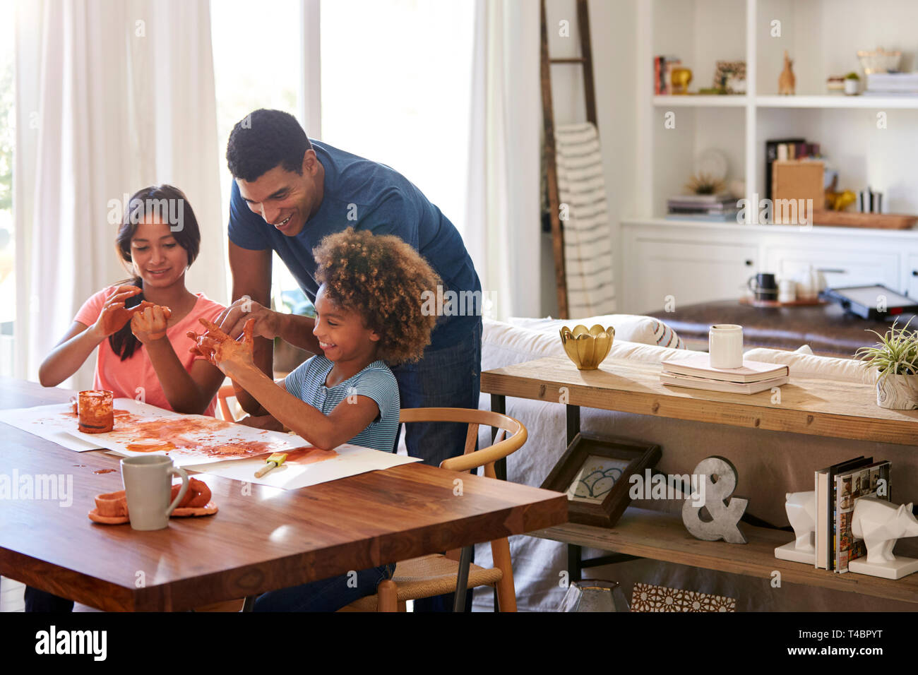 Papa millénaire aider sa fille et son amie jouer avec de la pâte à modeler à la table de la salle à manger Banque D'Images