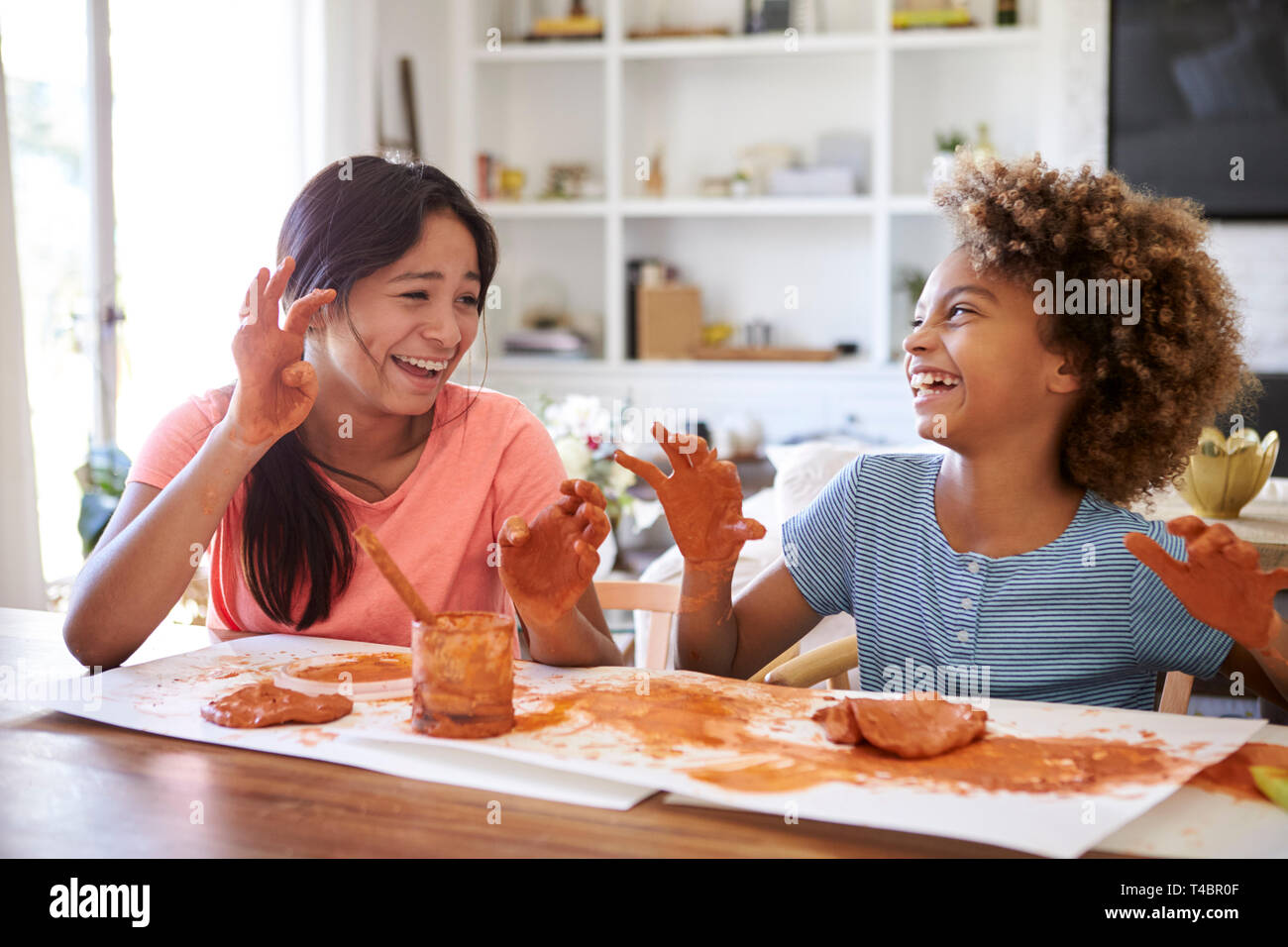 Deux copines s'amusant à jouer avec de la pâte à modeler à la maison, riant et montrant leurs mains sales à l'autre, Close up Banque D'Images