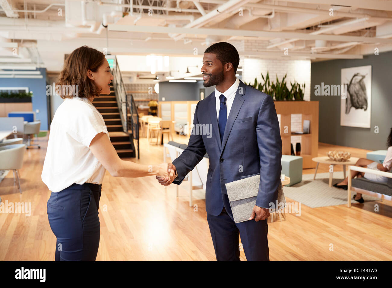 Businessman And Businesswoman Shaking Hands in Modern Open Plan Office Banque D'Images