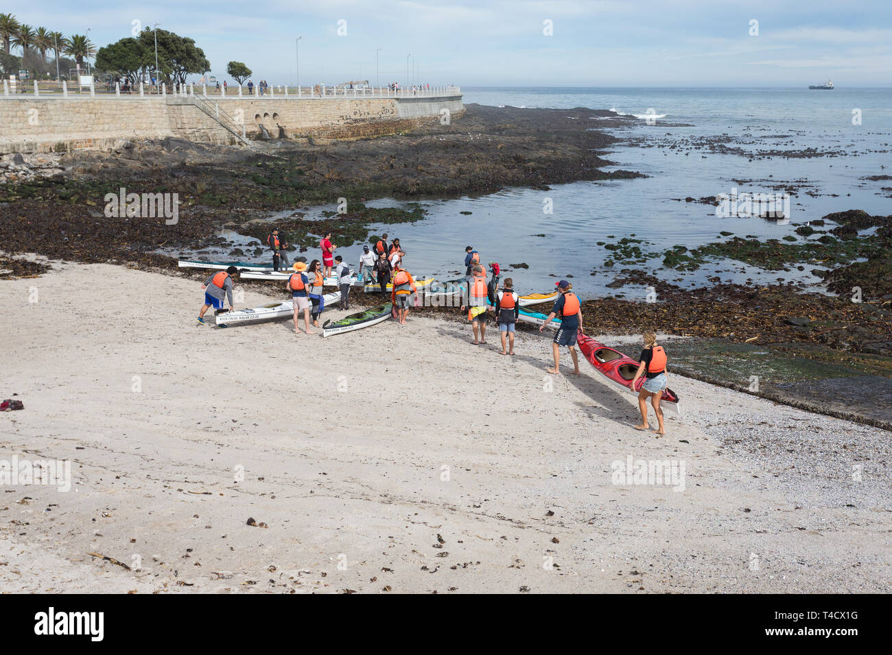 Groupe de touristes portent leurs kayaks jusqu'à la mer pour se préparer à une excursion sur l'océan à Sea Point, à Cape Town, Afrique du Sud, au cours de l'été Banque D'Images