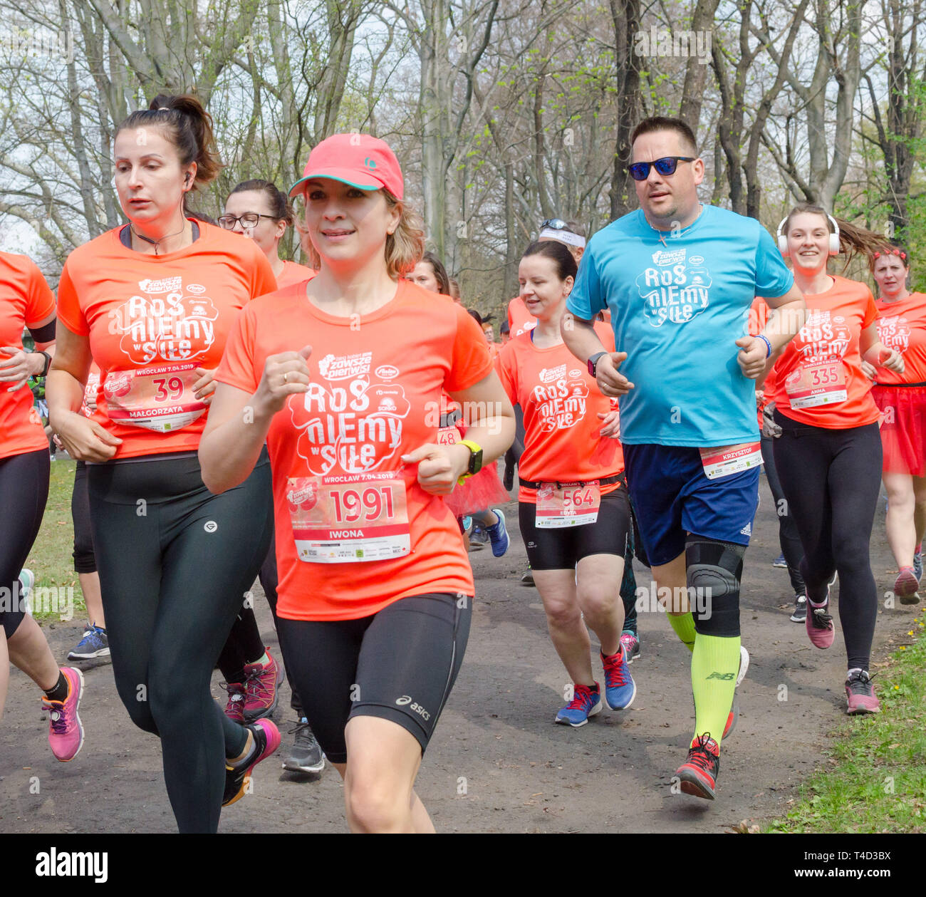 Grand groupe de femmes en orange t-shirts avec des chiffres et un homme en t-shirt bleu marathon s'exécute dans le parc au printemps. Wroclaw, Pologne, avril,7. Banque D'Images