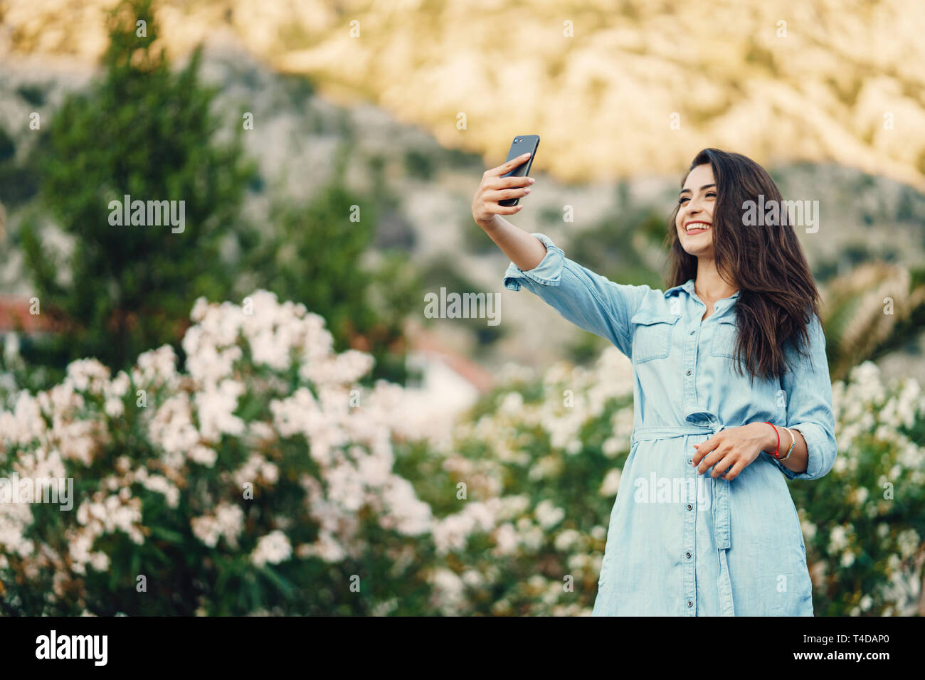 Une belle jeune fille dans une robe bleue, debout près de la fleur arbre et utiliser le téléphone Banque D'Images