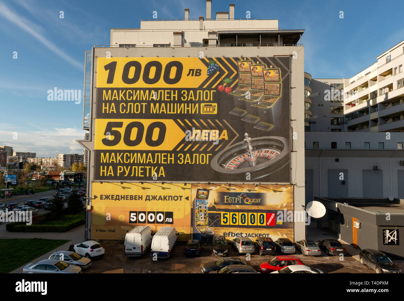 Europe de l'est environnements urbains laids comme voitures garées dans la terre par une publicité de mur de casino promettant de grands gains à Sofia, Bulgarie, UE Banque D'Images