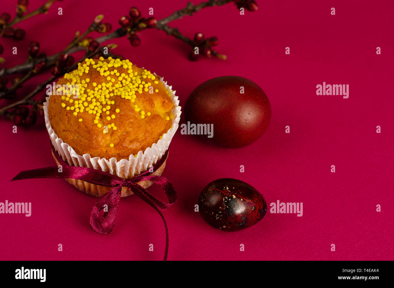Muffins de pâques décorés avec du ruban et des Sprinkles, les oeufs colorés et une branche d'arbre d'abricot sur un fond rose ou fuchsia. Copier l'espace. Greetin Banque D'Images