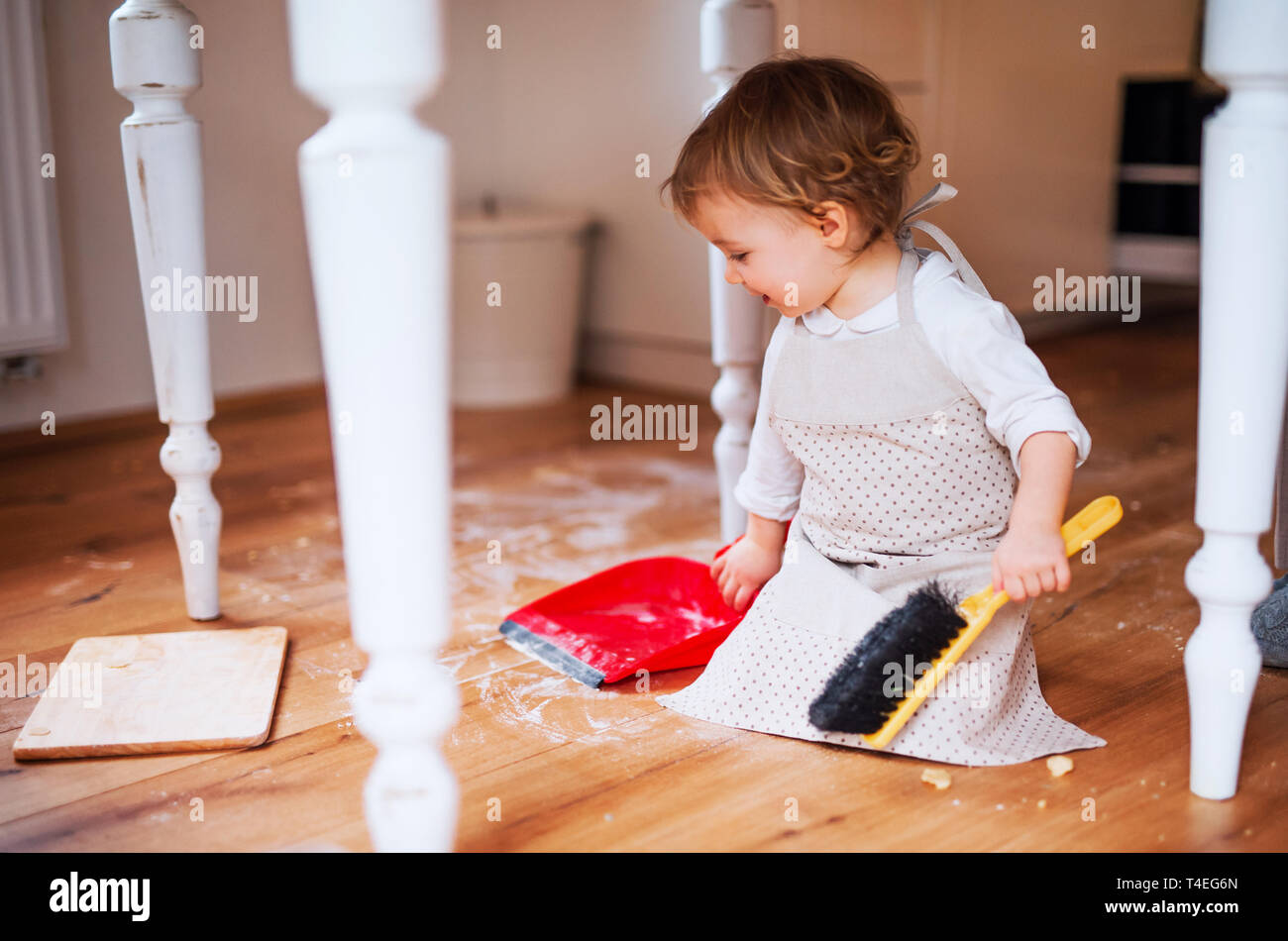 Un petit bébé fille avec un balai et un porte-poussière balayer plancher  malpropre dans la cuisine à la maison Photo Stock - Alamy