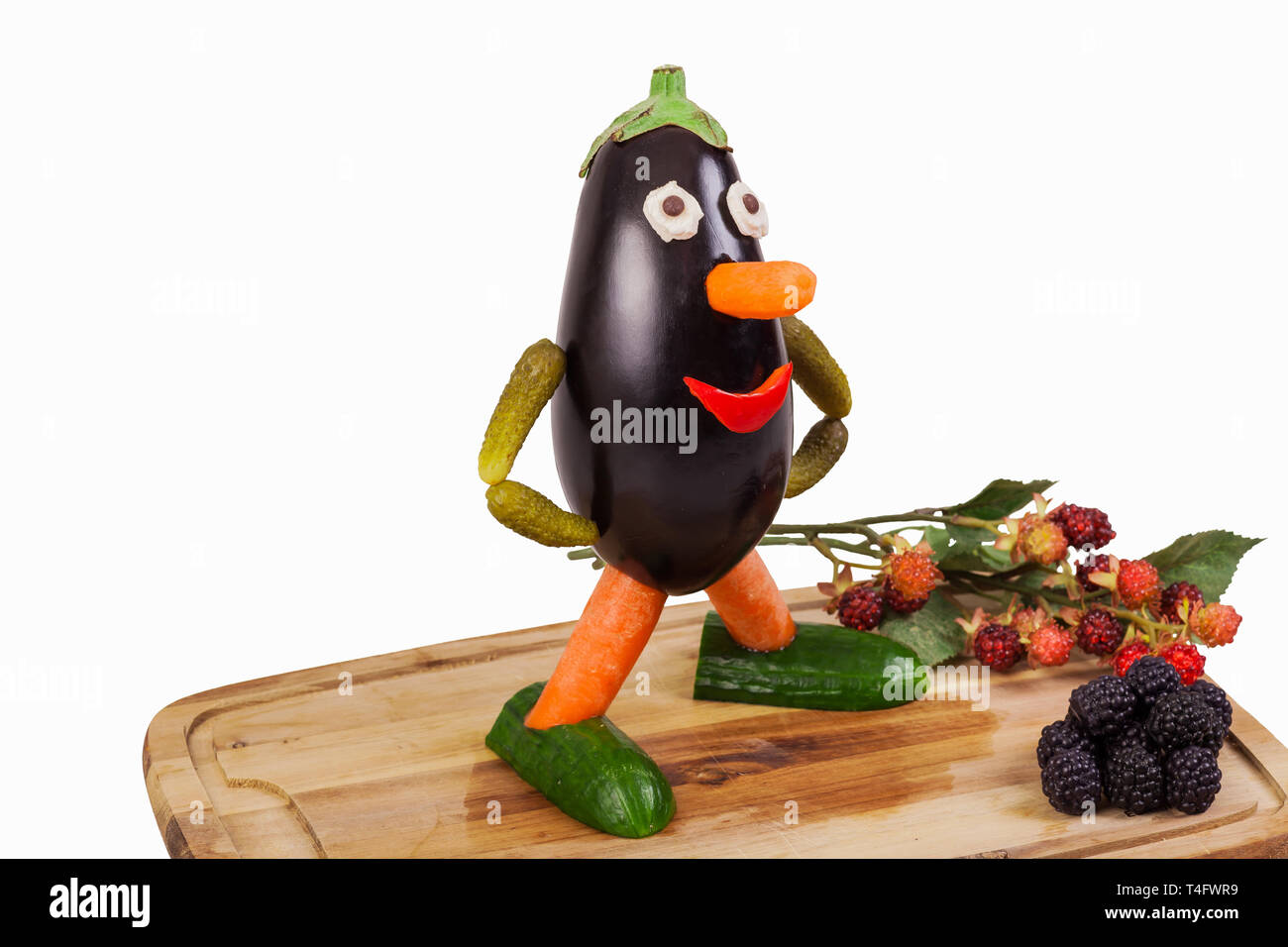 Funny figure taillée d'une aubergine avec deco fruits sur une planche en bois isolé- Banque D'Images