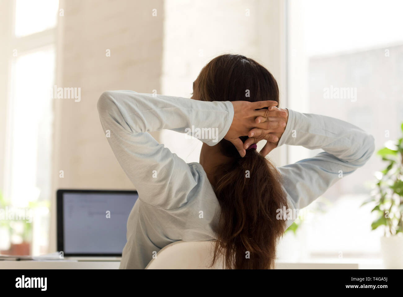 Woman relaxing on président au travail holding hands behind head Banque D'Images