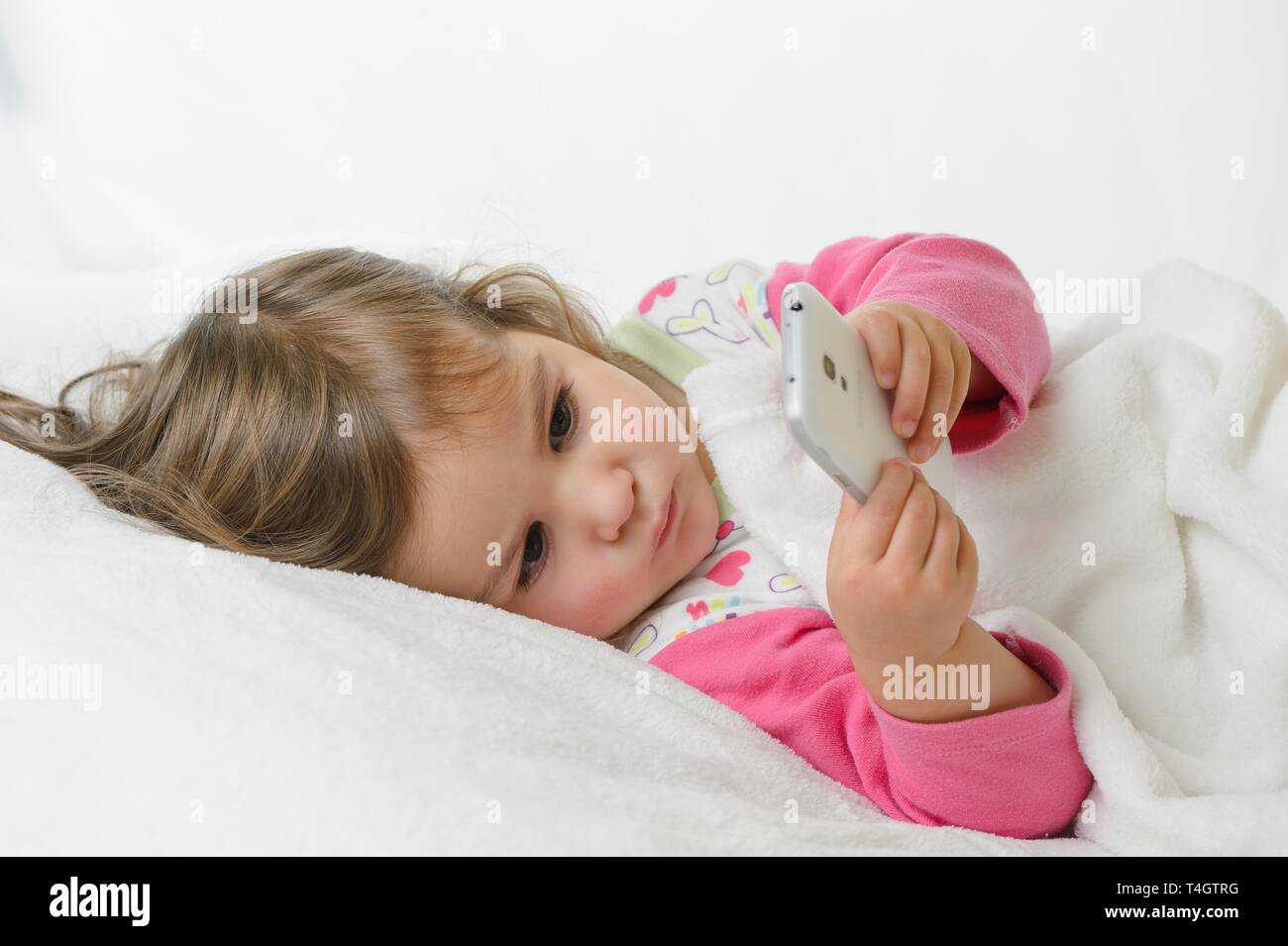 Fille, 2 ans, portrait, couchant avec téléphone mobile, Allemagne Banque D'Images