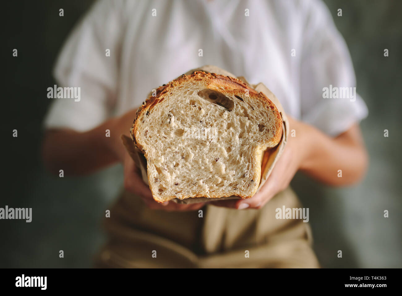 Baker femmes debout à la boulangerie et la tenue du pain frais. Close up of a female baker tenant un pain dans une boulangerie. Banque D'Images