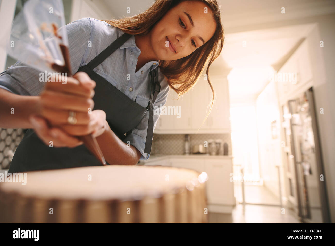 Femme pastry chef decorating un gâteau avec du chocolat en cuisine. Femme portant un tablier, faire un délicieux gâteau à la maison. Banque D'Images