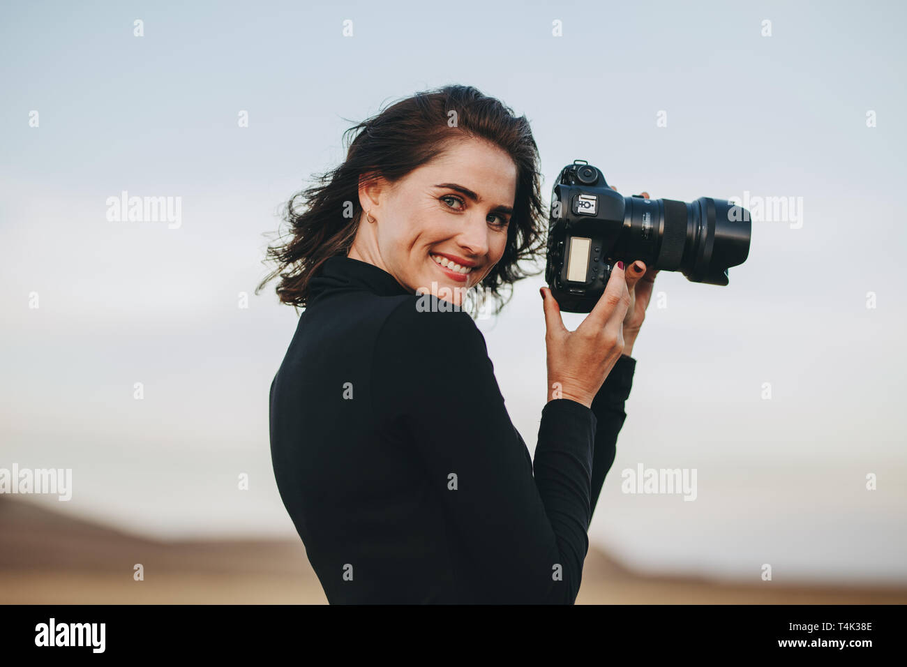 Photographe positifs bénéficiant des prises de vue en extérieur photo. Young woman in casual tenant une caméra photo et souriant. Banque D'Images