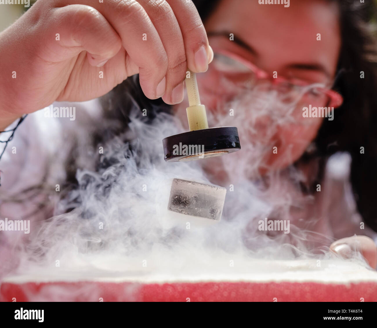 Femme élève démontre la lévitation magnétique quantique et l'effet de suspension. Une touche de l'azote liquide refroidit un supraconducteur céramique forcer t Banque D'Images