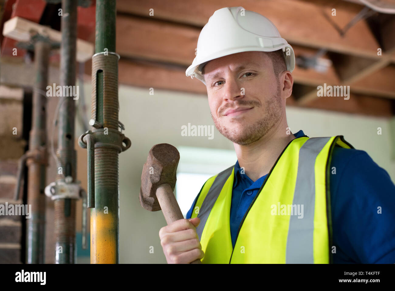 Portrait of Construction Worker With Sledgehammer démolir Mur dans maison rénovée Banque D'Images
