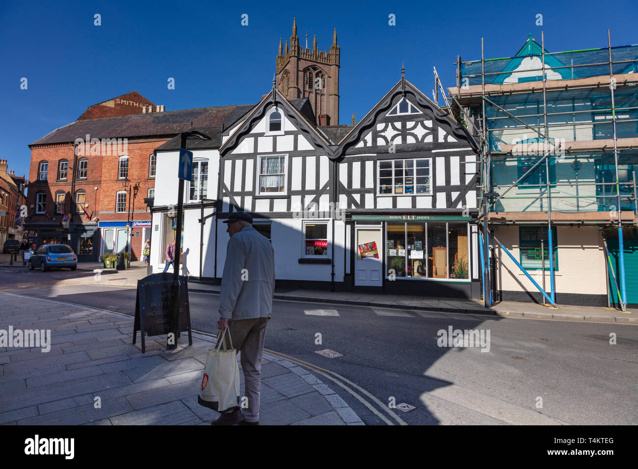 Un homme âgé portant un sac shopping promenades dans l'ombre sur la rue King, Ludlow, Shropshire, Angleterre Banque D'Images