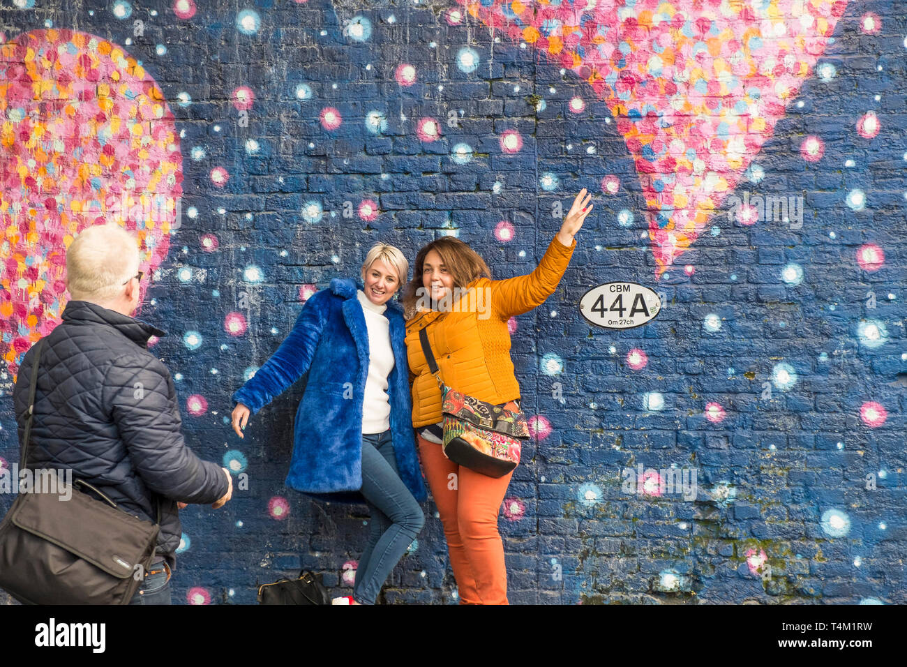 Les amis posant pour une photo contre une grande murale colorée peinte sur un mur à Londres. Banque D'Images