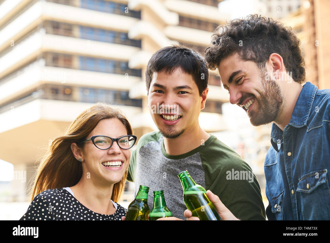 Trois jeunes étudiants comme célébrer une fête et toast avec une bouteille de bière Banque D'Images
