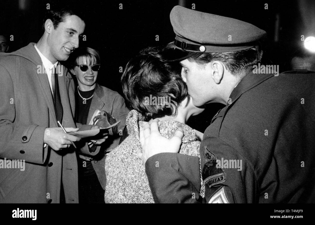 Adolescent Américain idol Elvis Presley (r) embrasse l'une de ses femmes d'admirateurs en face de journalistes sur la joue sur le 1er mars en 1960. La jeune fille a réussi à saisir le Ray barracks à Friedberg sous prétexte d'être un journaliste, où la conférence de presse à l'occasion de la résiliation de Presley's service militaire a eu lieu. L'American Rock'n Roll singer a été stationné à Friedberg (Hesse) dans le cadre de son service militaire dans l'armée américaine dans les années 1950 et quittera l'Allemagne de Francfort-sur-le Main dans un avion militaire le 2 mars en 1960. Dans le monde d'utilisation | Banque D'Images