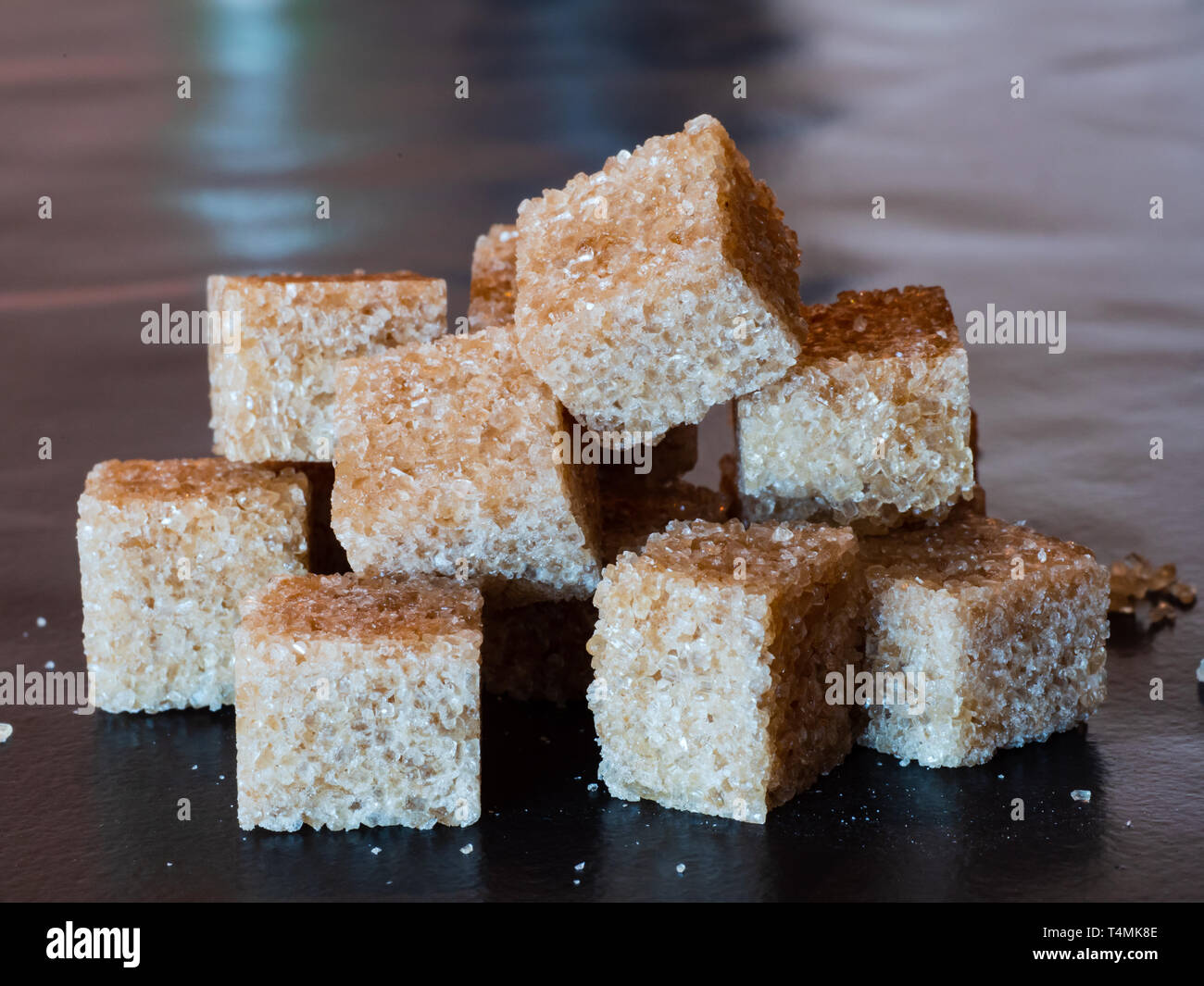 Tas de cubes de sucre brun sur une surface noire. Banque D'Images