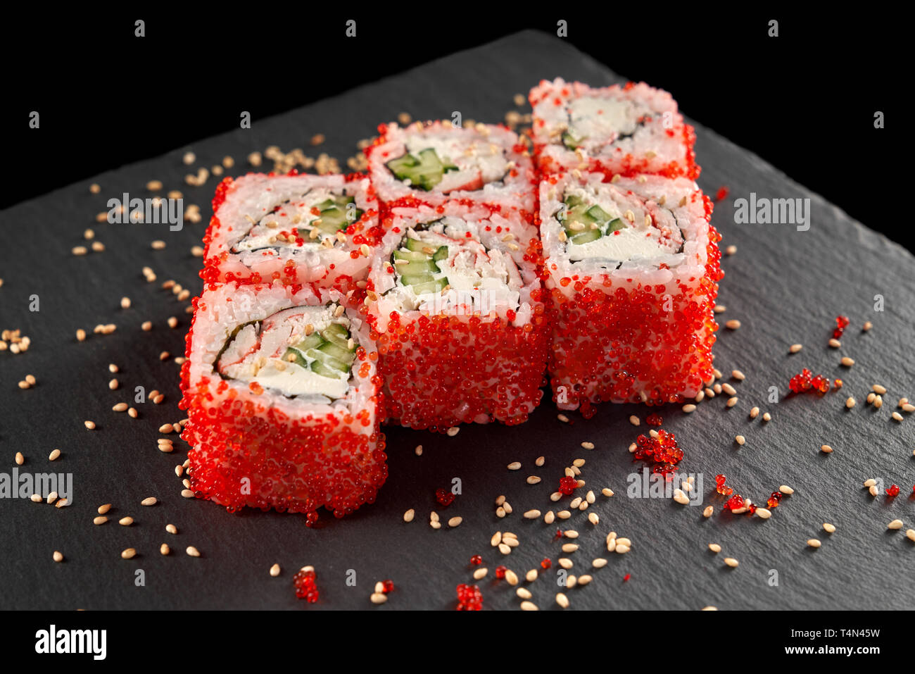 Sushi Uramaki servi sur plaque de pierre noire, décoré avec du sésame. California roll rempli de concombre, fromage à la crème et la chair de crabe, couverts d'oeufs de tobiko. Banque D'Images