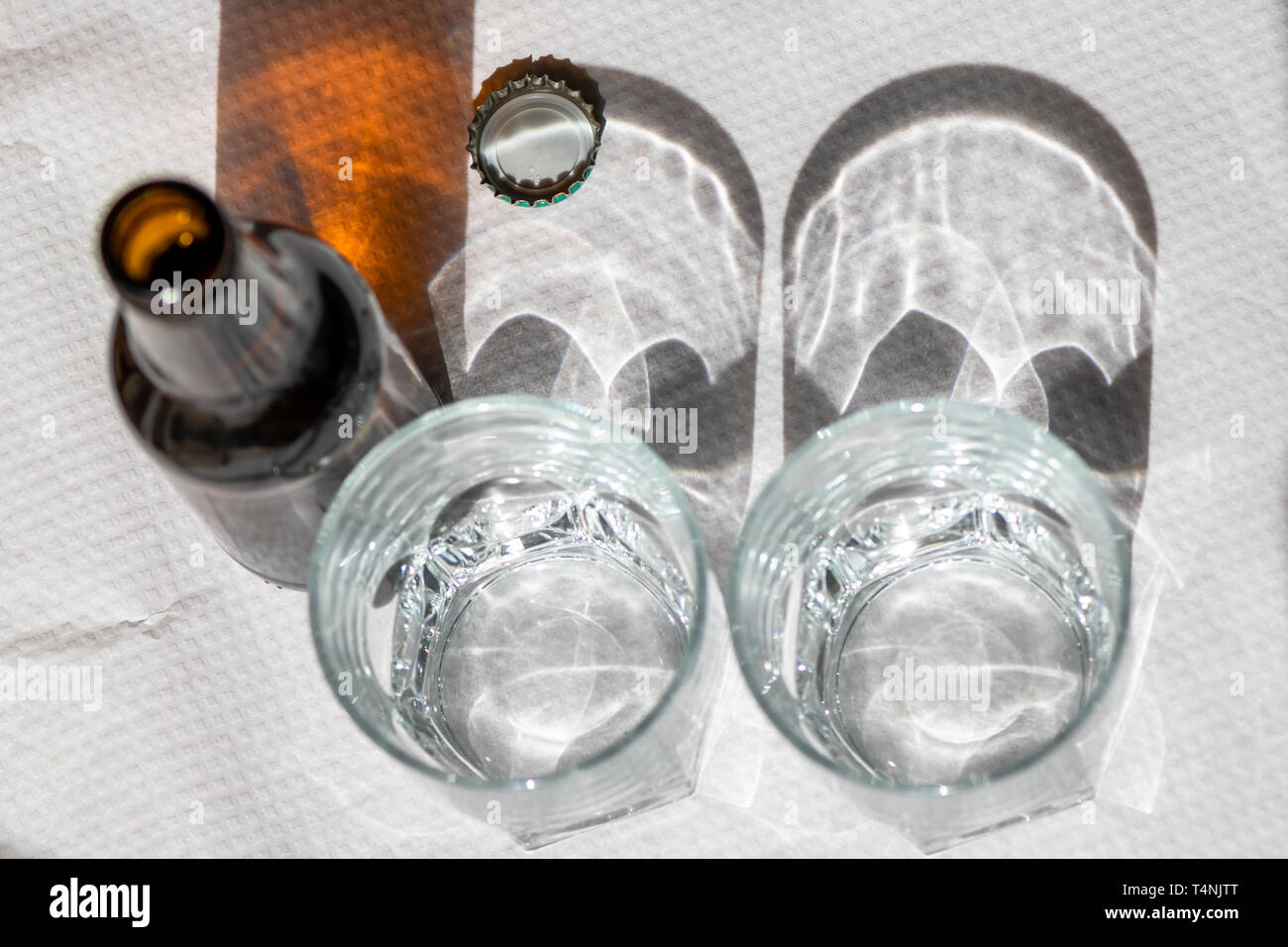 Deux verres de cristal et une bouteille de bière sur une nappe en papier blanc. Scène ensoleillée avec des ombres. Concept- partager. Banque D'Images