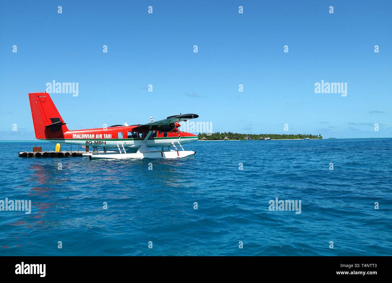 Un hydravion rouge de Maldivian Air Taxi est posé sur la magnifique mer bleu ouvert avec une petite île dans l'arrière-plan. Banque D'Images