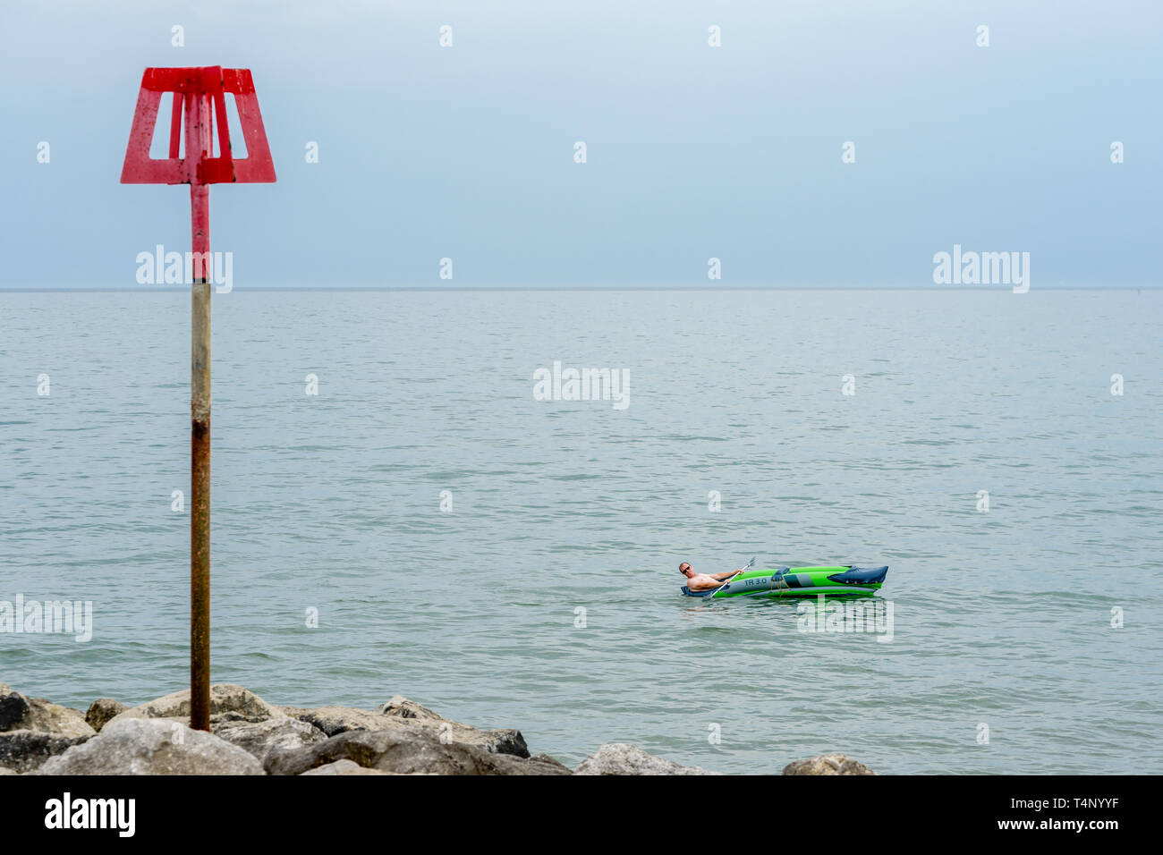 Un homme qui profite du temps chaud dans un bateau gonflable le long de la plage de Highcliffe à Dorset, Angleterre, Royaume-Uni. Banque D'Images